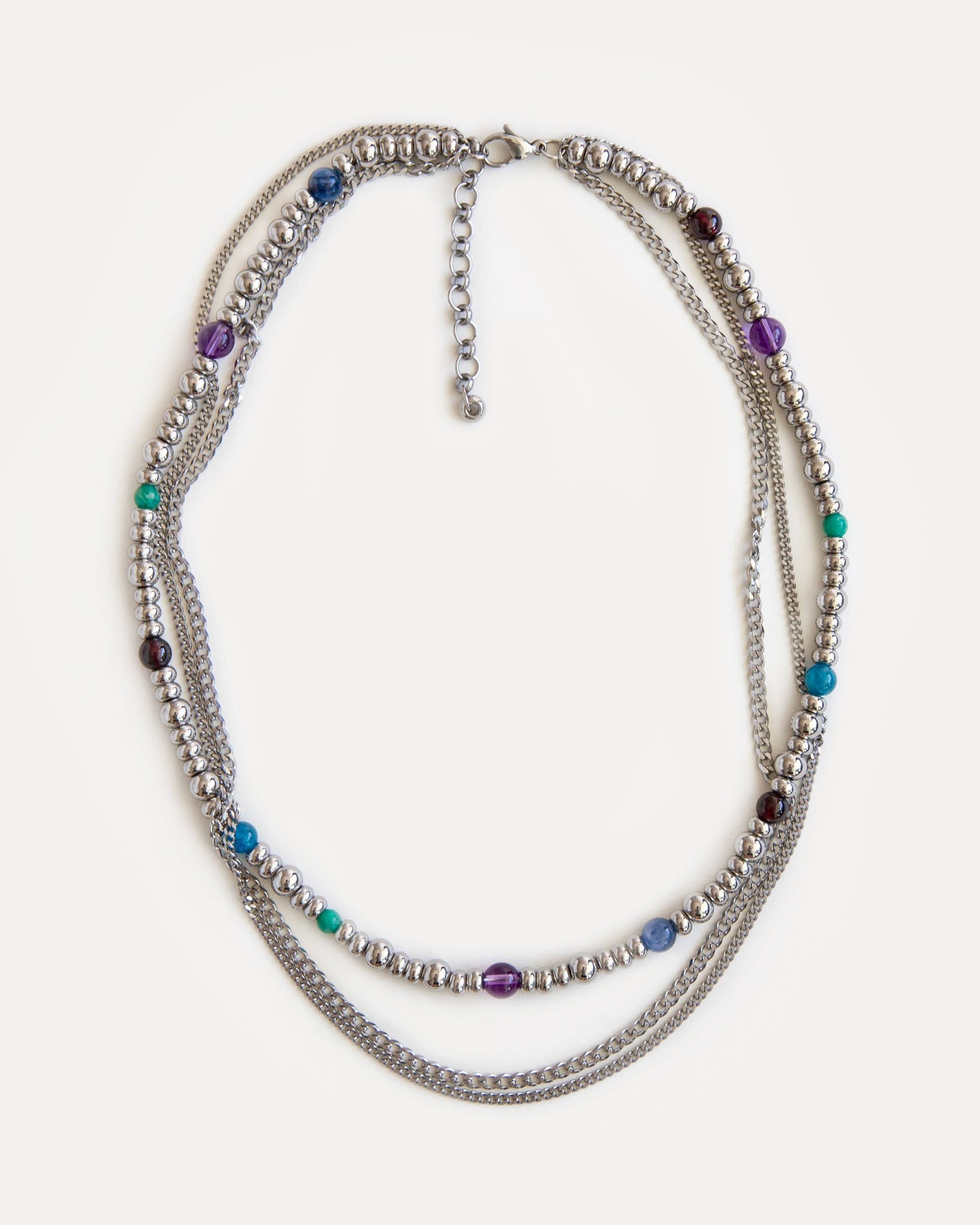 Full view of the GEMS necklace, a sophisticated three-layer design of durable jewelry steel chains and vibrant natural gemstones: garnet, amethyst, kyanite, amazonite, and apatite. Laid flat, the necklace displays its elegant symmetry and playful color combination, making it a versatile statement piece for any wardrobe. Explore Jewell Reef's unique, handcrafted fashion jewelry, perfect for layering or as a standalone gift.