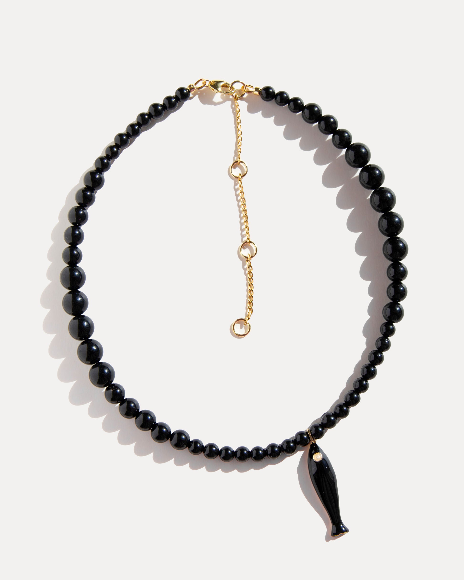 Black agate necklace with ceramic fish pendant and gold-plated clasp photographed on white background