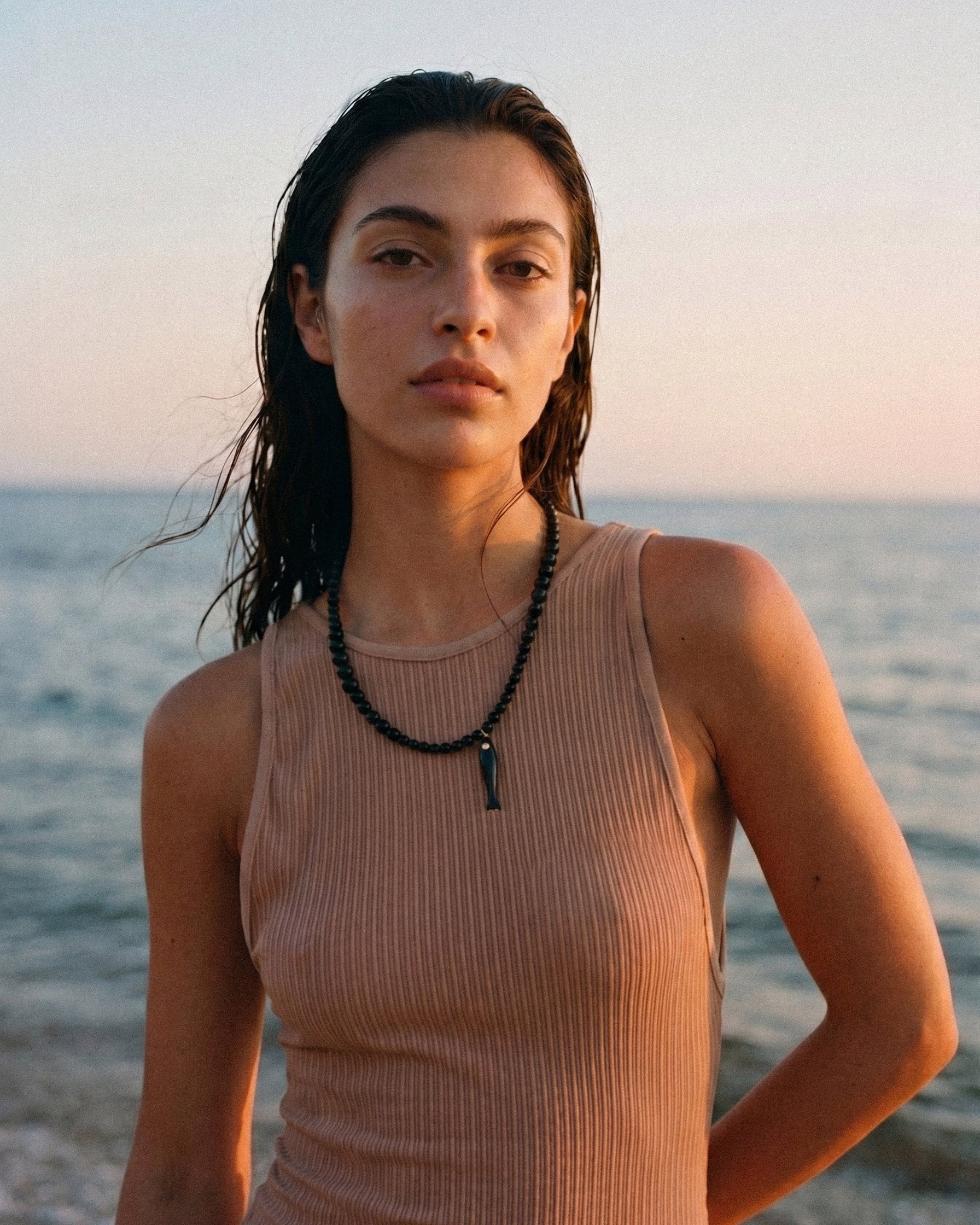 Model wearing black agate necklace with ceramic fish pendant by the sea at sunset