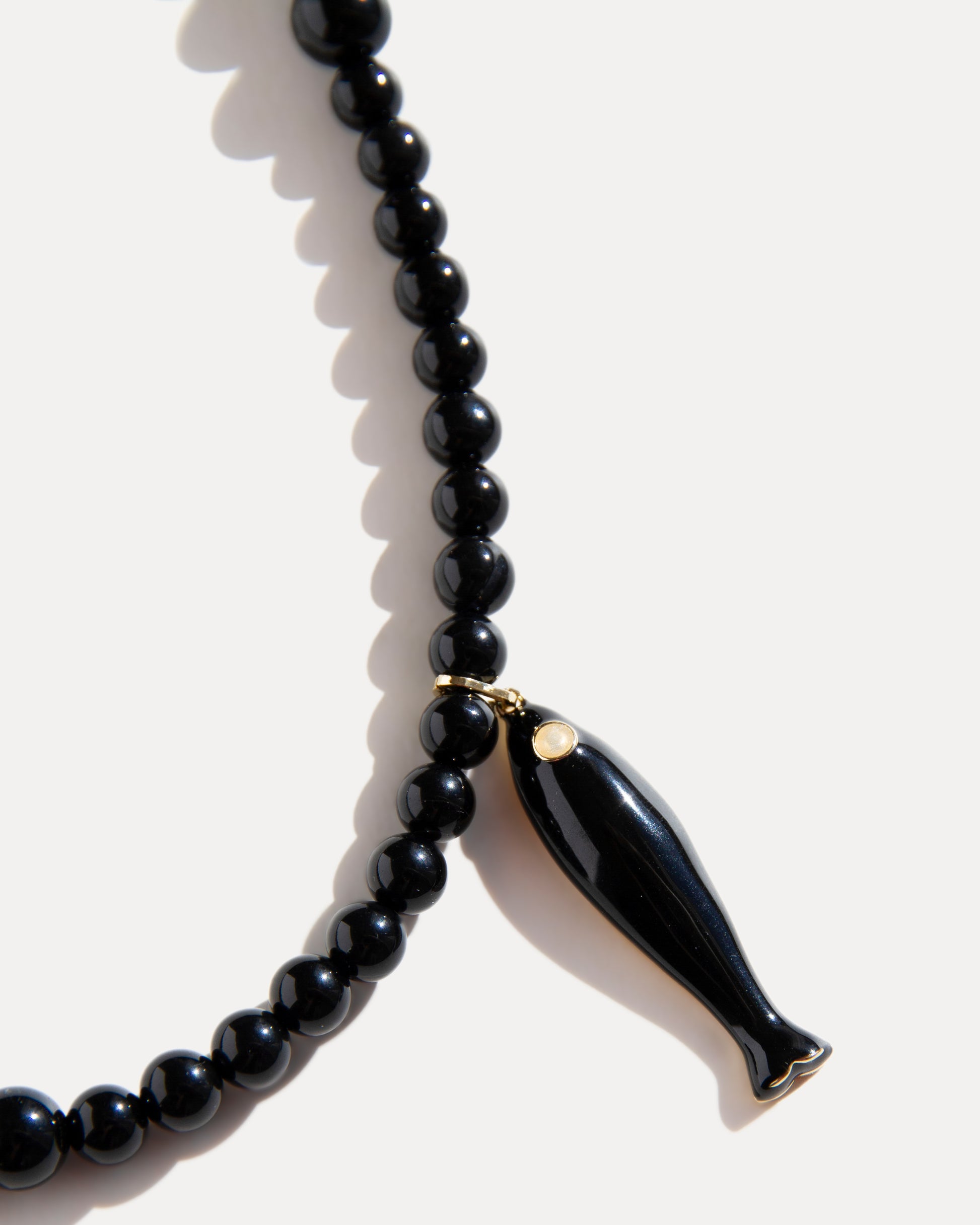 Close-up of black agate necklace with glossy ceramic fish pendant and gold-plated details on white background