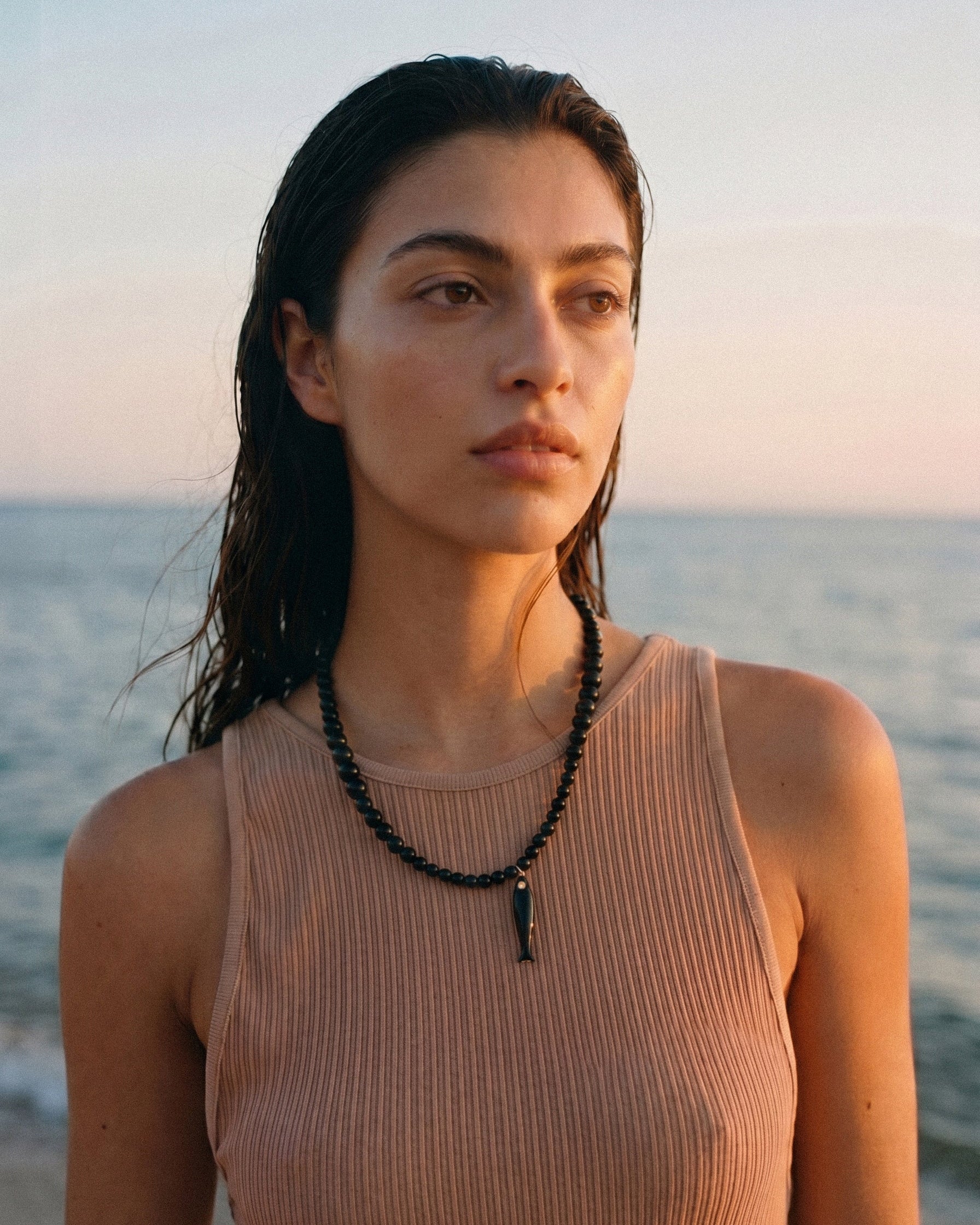Model wearing black agate necklace with ceramic fish pendant and gold details, asymmetrical coastal jewelry inspired by evening swims