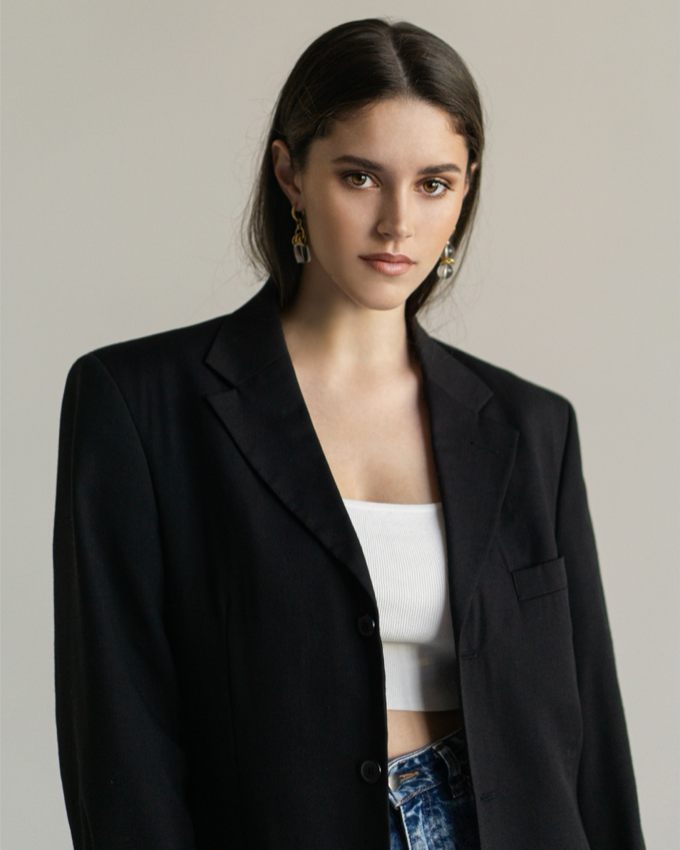 Asymmetric gold-plated statement earrings with clear quartz, styled with a black blazer and white top for a bold, modern and elegant look.