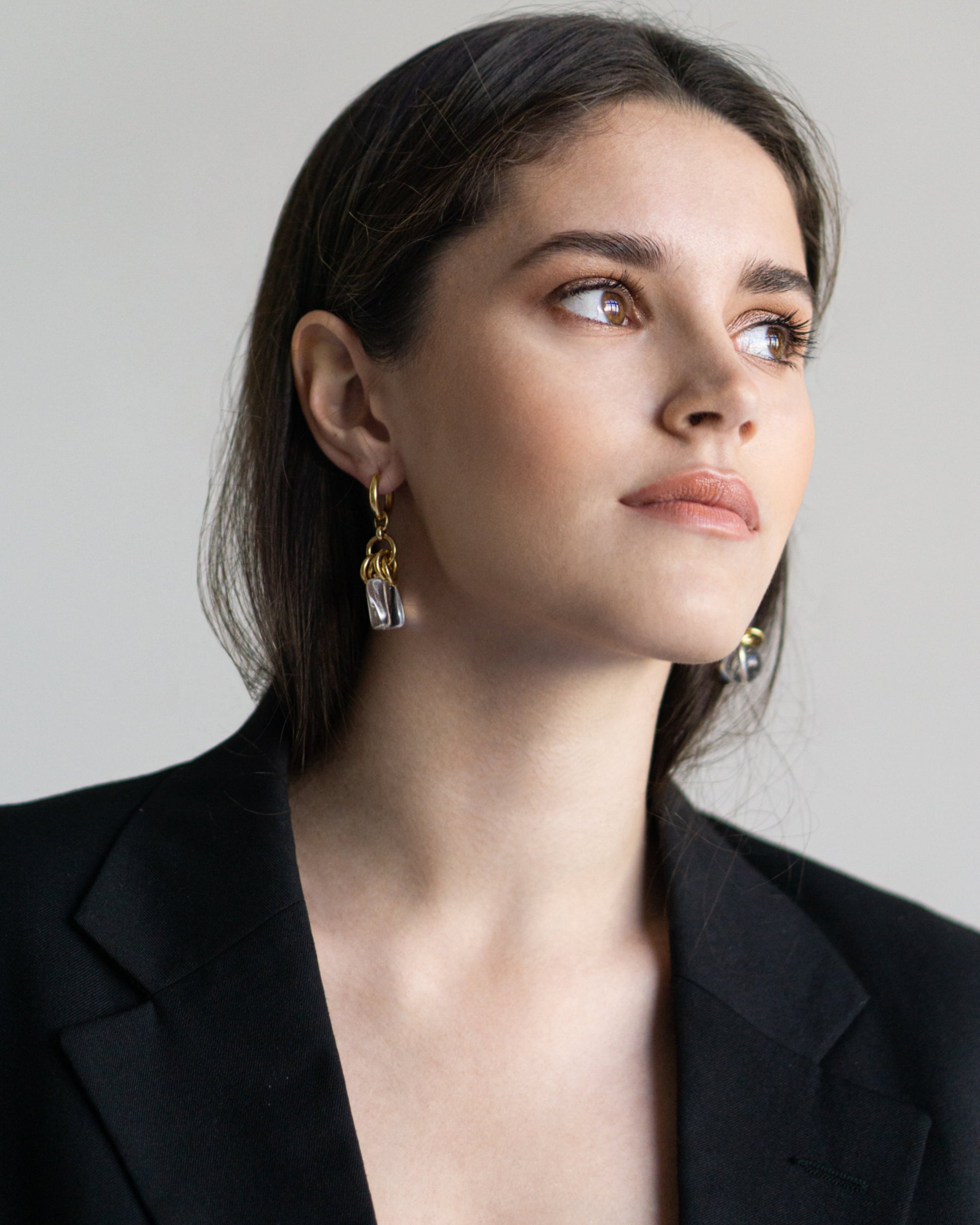 Close-up of asymmetric Nora Earrings with clear quartz and gold-plated brass, bold statement jewelry with sculptural form and modern elegance.