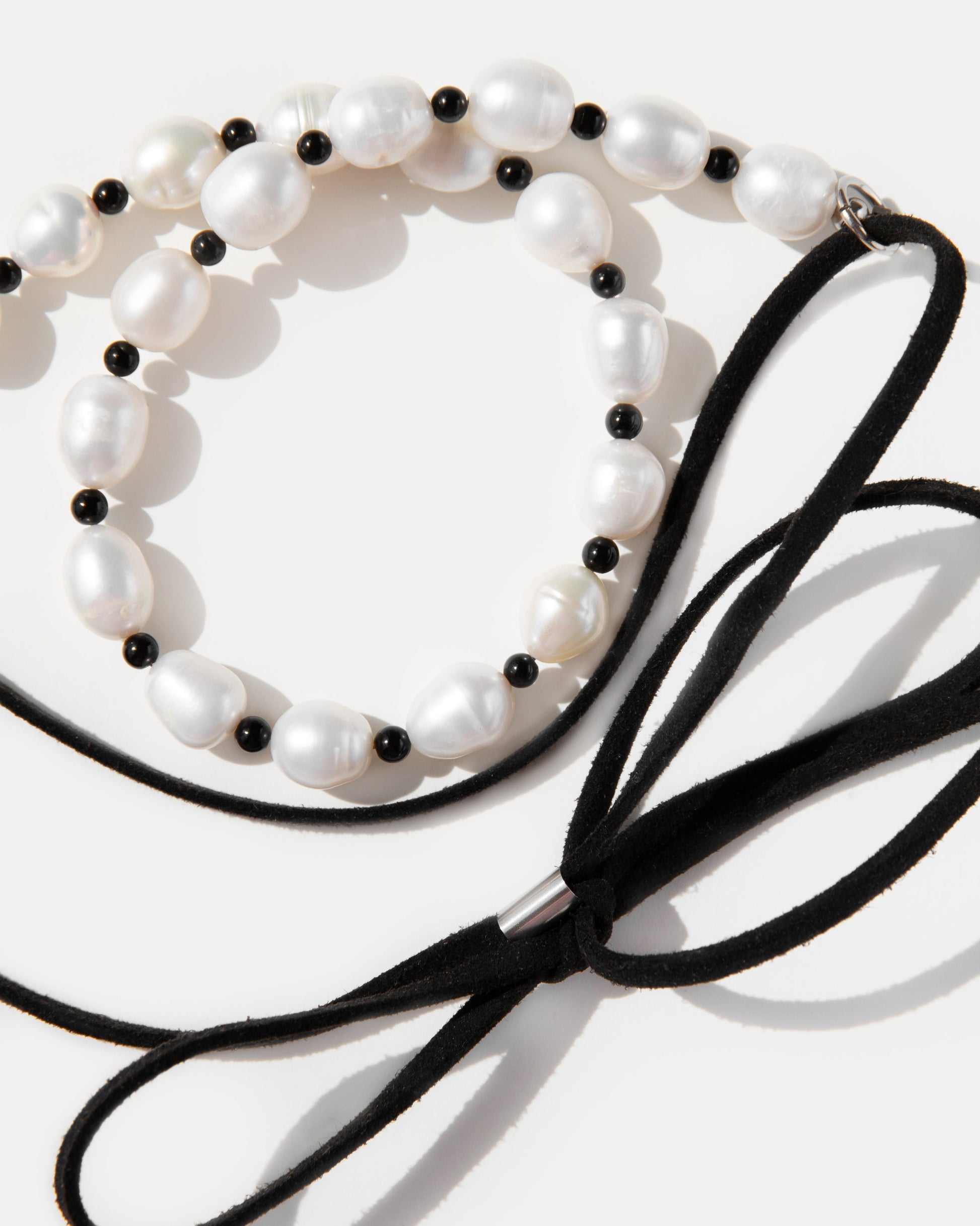 Close-up of Pearl Mademoiselle Necklace with freshwater pearls, black agate, and suede bow tie detail.