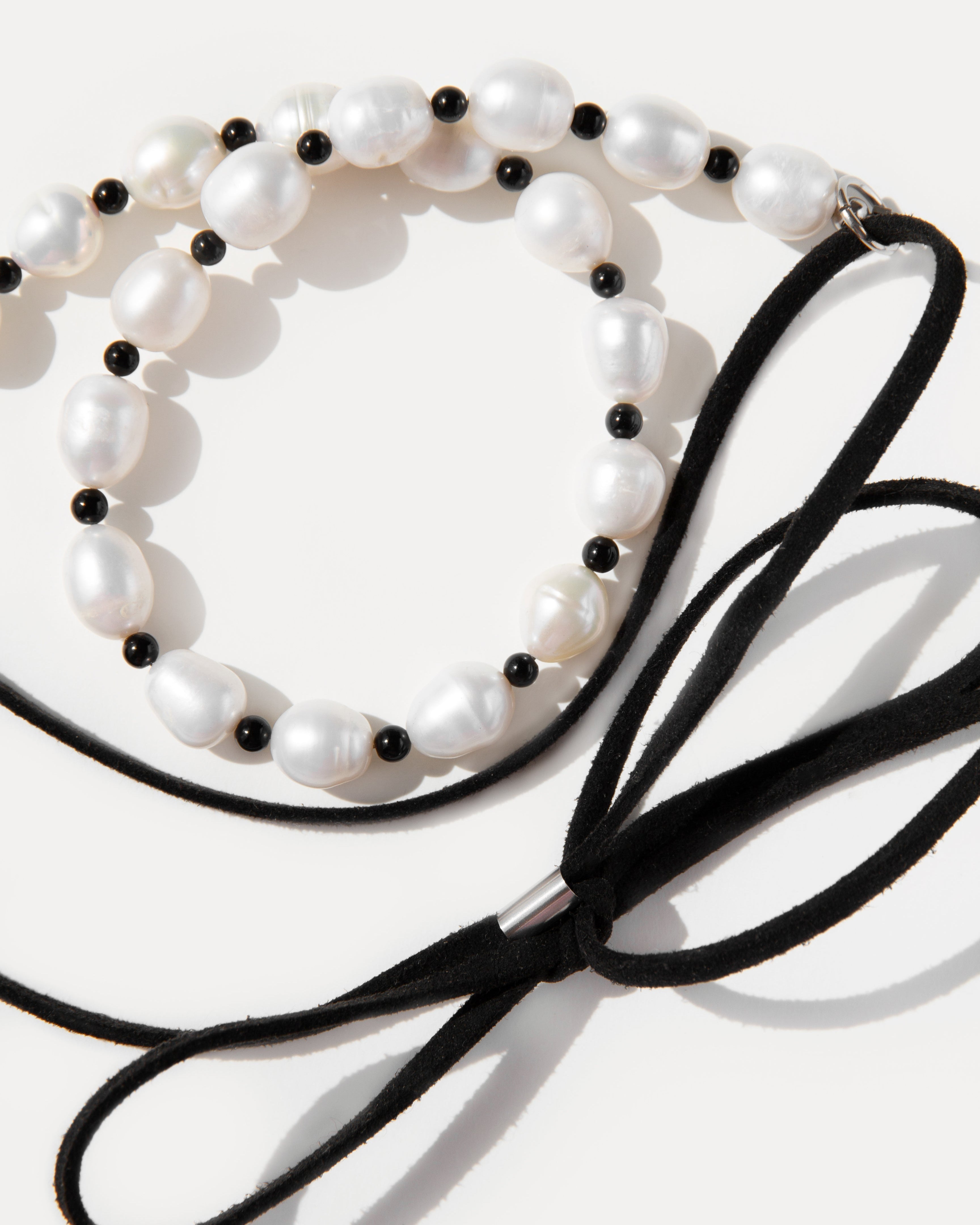 Close-up of Pearl Mademoiselle Necklace with freshwater pearls, black agate, and suede bow tie detail.