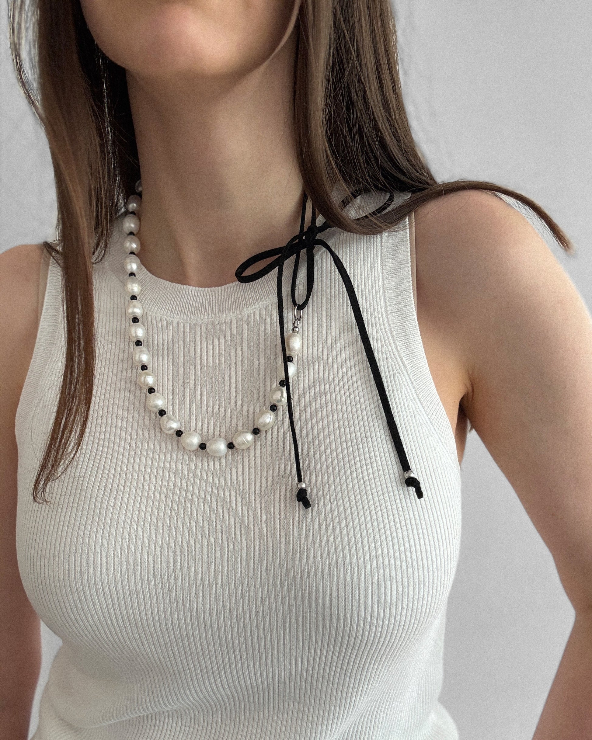 Pearl Mademoiselle Necklace with freshwater pearls, black agate, and a suede tie worn long for an elegant, feminine look.