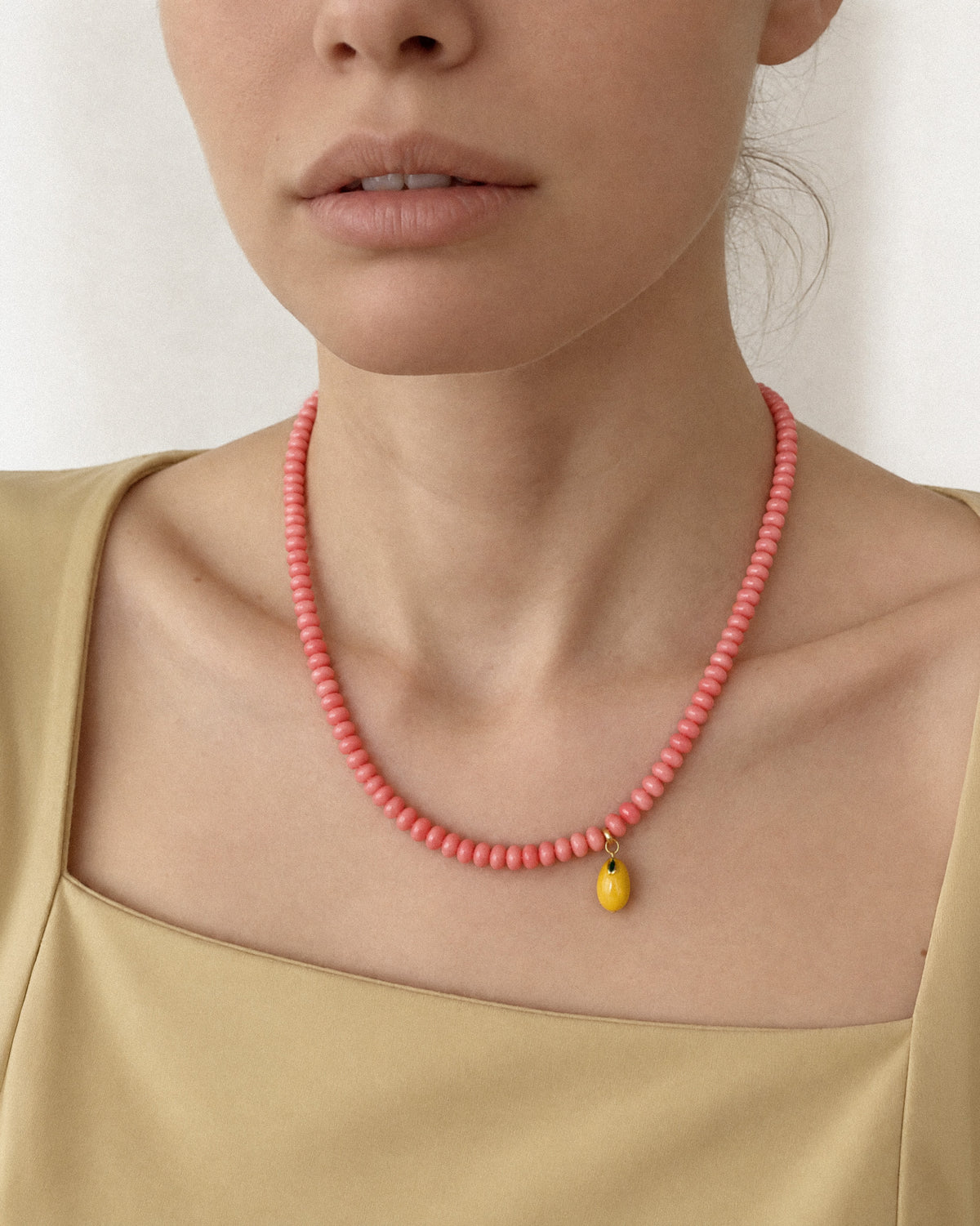 Model wearing the Pink Sorbet Necklace as a short pink coral choker with a small yellow lemon charm.