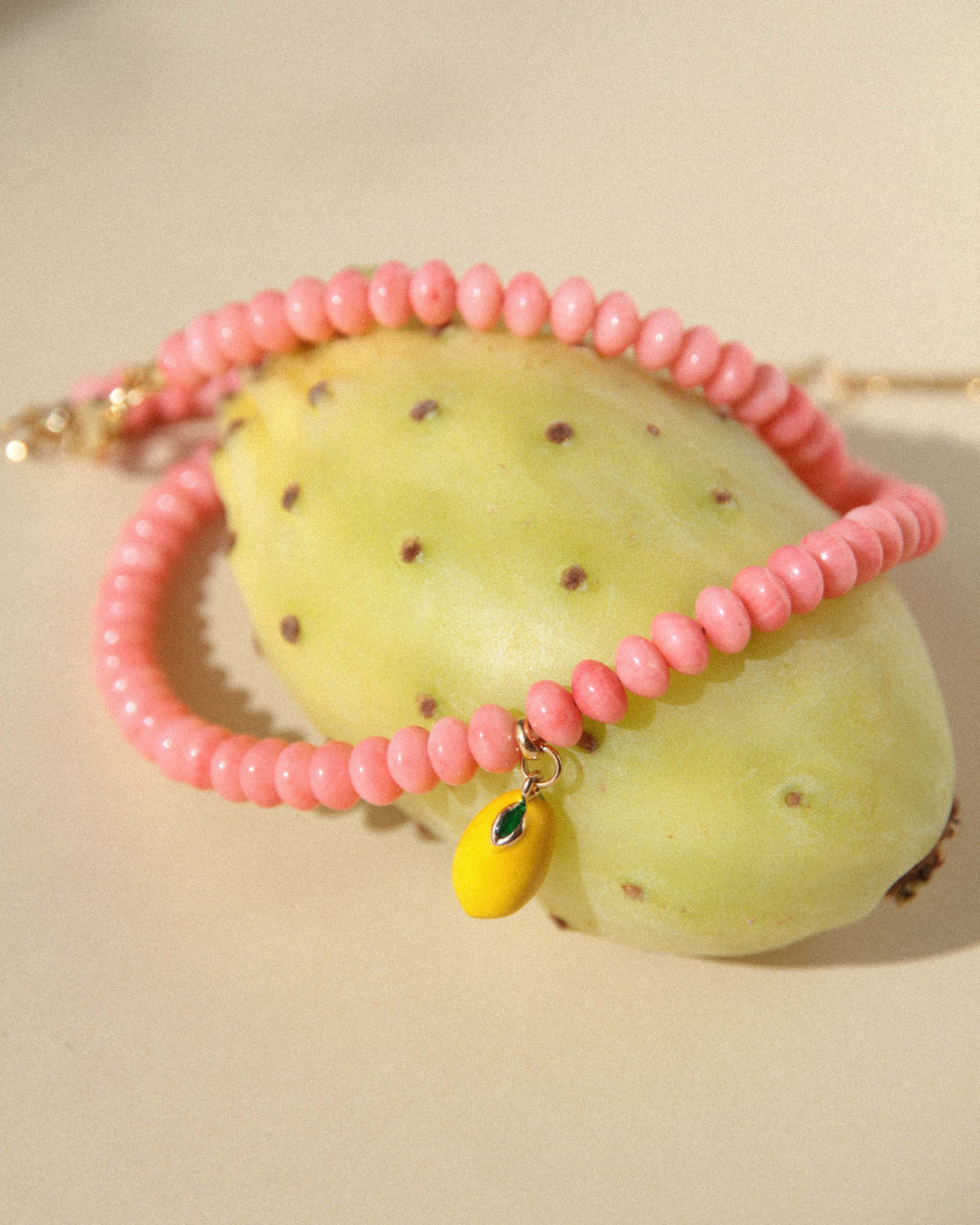 Pink coral bead necklace wrapped around a yellow cactus fruit with its enamel lemon charm in view.
