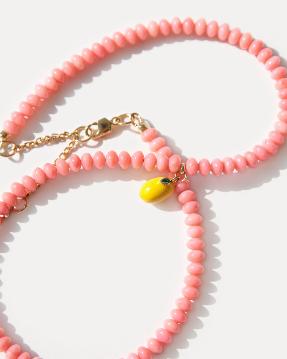 Close-up of pink coral beads, a yellow enamel lemon charm and 18K gold-plated brass details.