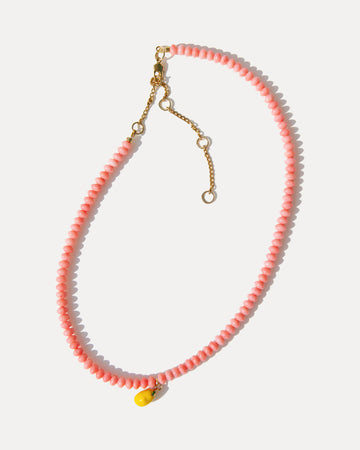 Pink coral bead necklace with a yellow enamel lemon charm and gold-plated extender chain on a white background.