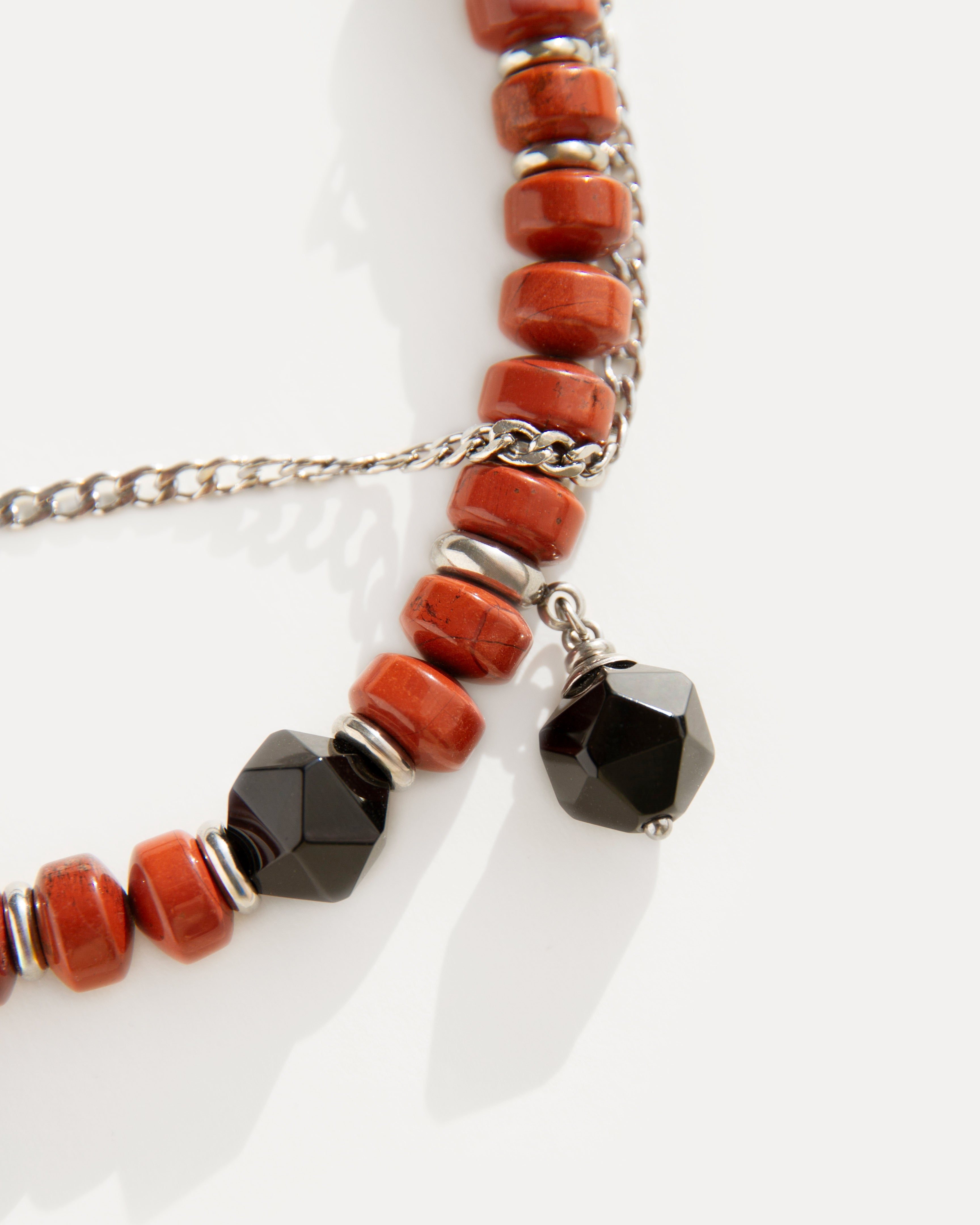 Detail view of the Red Outline Bracelet with terracotta jasper beads, faceted black agate charm, and stainless steel chain in geometric balance.