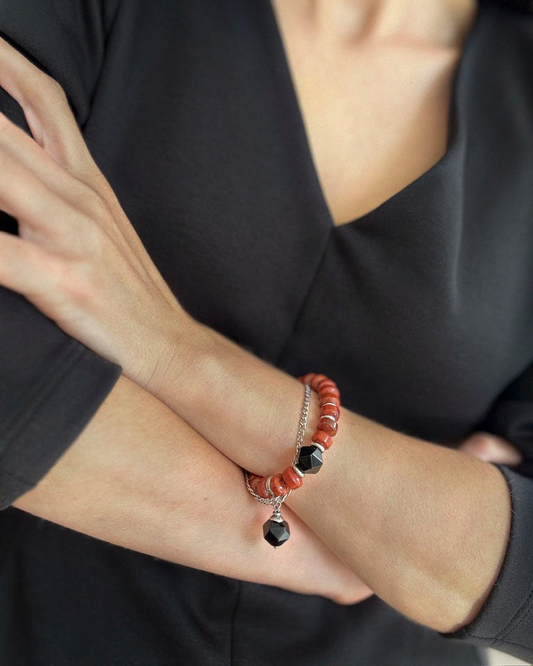 Red Outline Bracelet styled on wrist, featuring terracotta jasper beads, faceted black agate charms, and stainless steel chain with bold contrast.