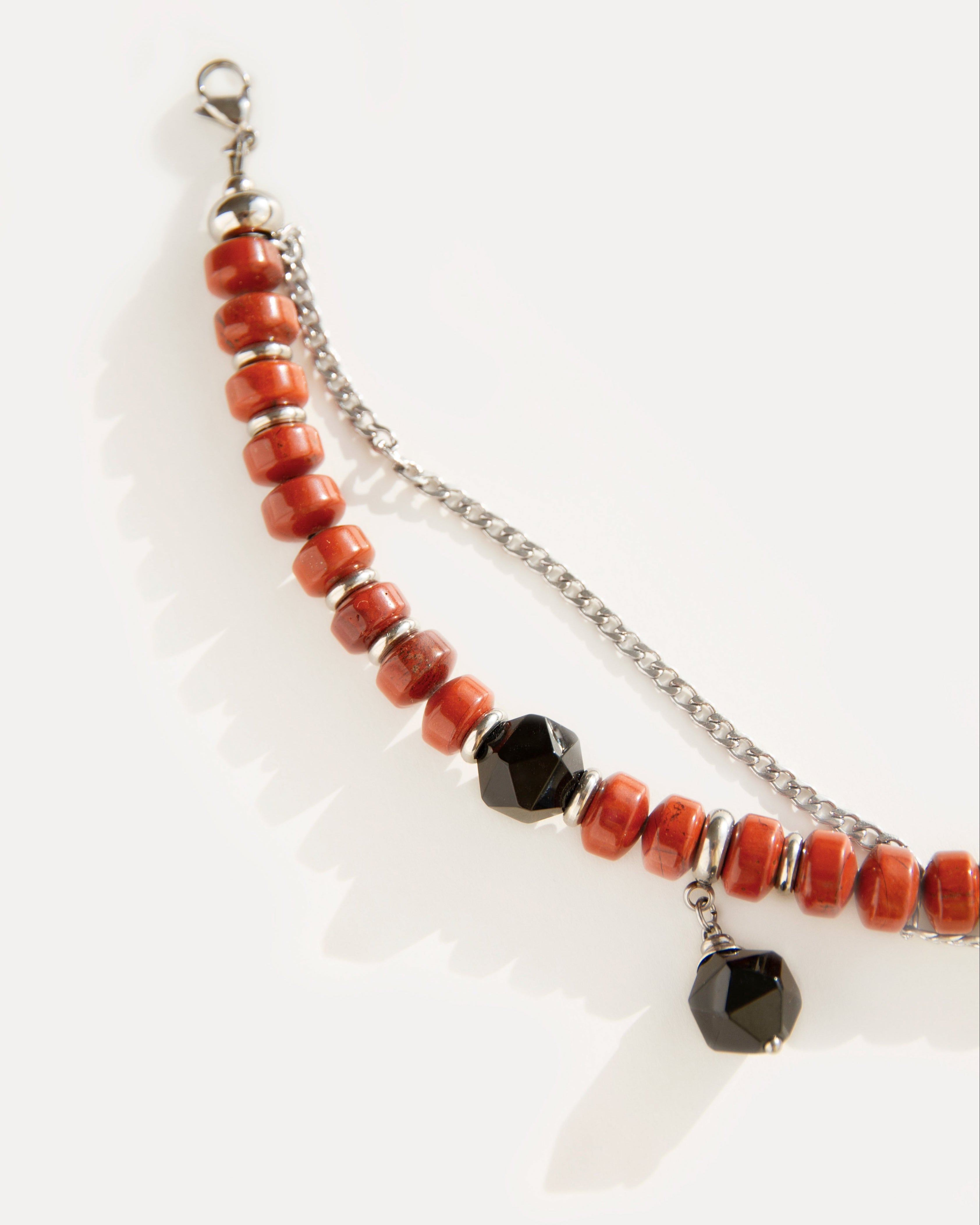 Close-up of the Red Outline Bracelet with terracotta jasper beads, faceted black agate, and stainless steel chain, bold yet refined design.