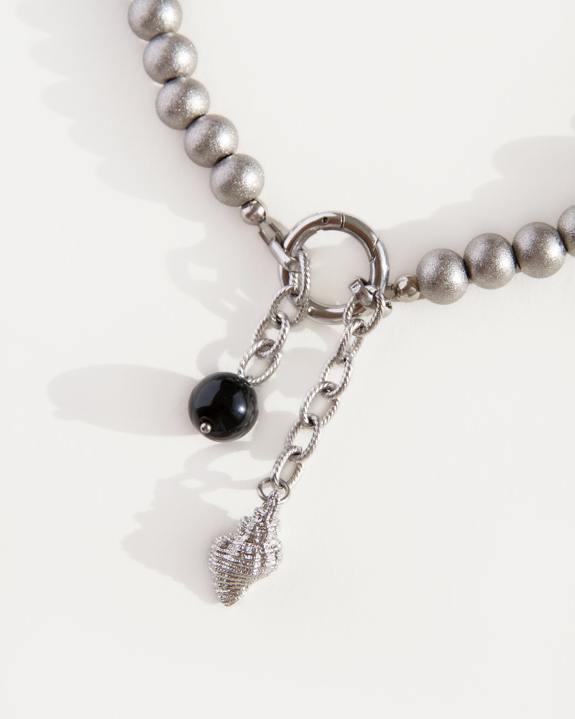 Close-up of black agate bead and shell pendant hanging from front ring clasp on stainless steel beaded choker necklace