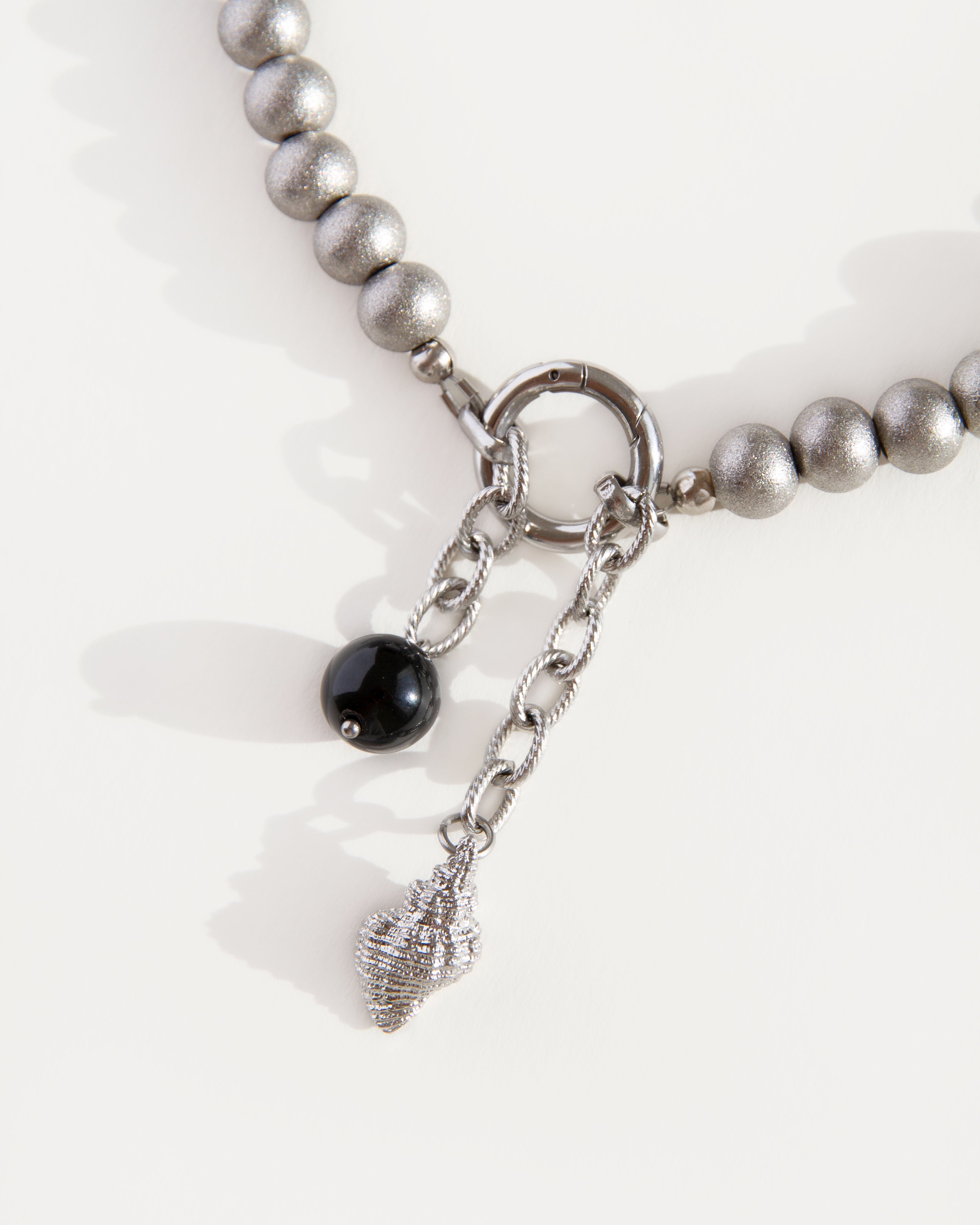 Close-up of black agate bead and shell pendant hanging from front ring clasp on stainless steel beaded choker necklace