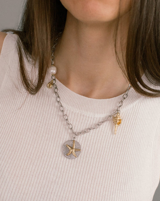 Sea Gifts Necklace styled on model — bold silver chain with starfish, shell and pearl charms. A modern mixed metal statement necklace for layering or solo wear.