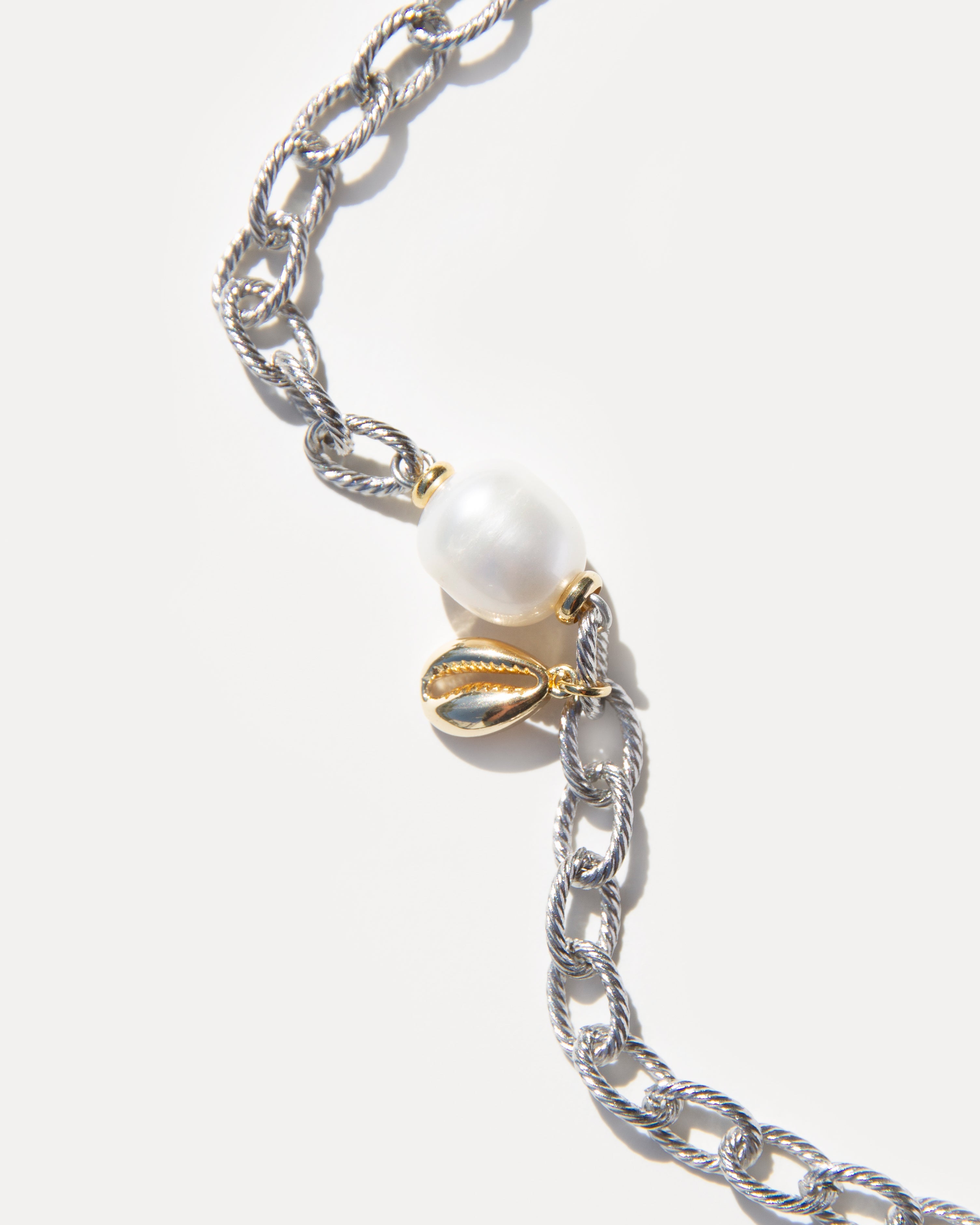 Close-up of Sea Gifts Necklace showing freshwater pearl and gold-plated shell charm on silver chain. Mixed metal design blends elegance with coastal inspiration.