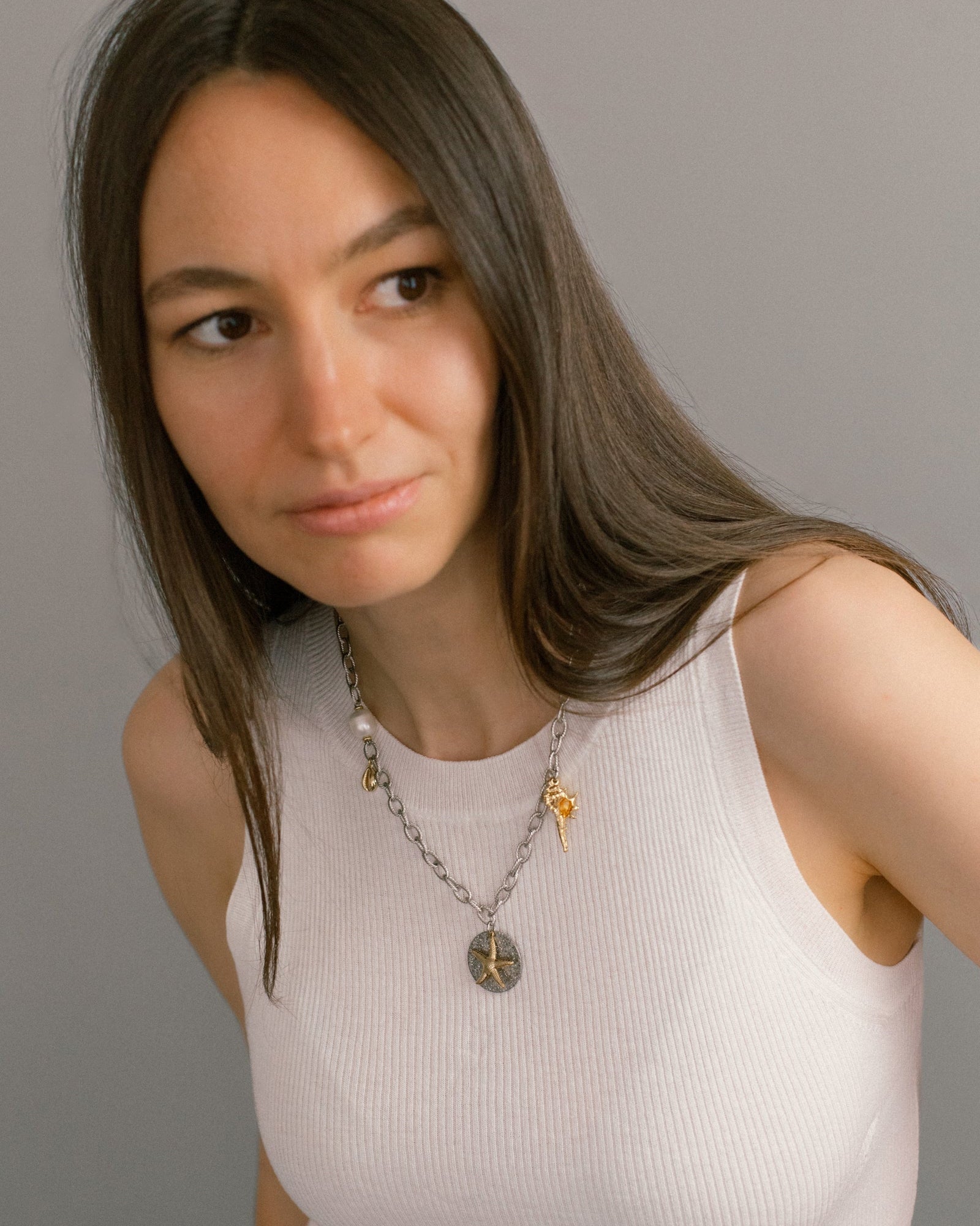 Sea Gifts Necklace worn with casual white top — mixed metal chain with pearl, starfish and shell charms. A versatile statement necklace for modern style.