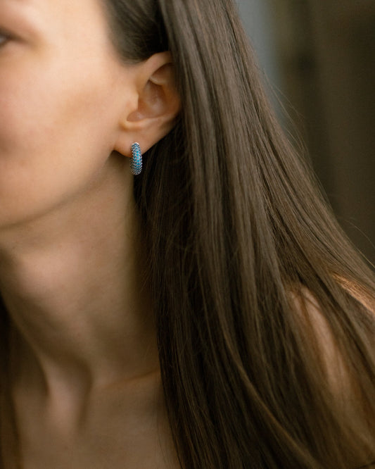 Blue cubic zirconia hoop earrings on model. Elegant mini hoops in silver-tone brass add modern sparkle and effortless shine to any look.