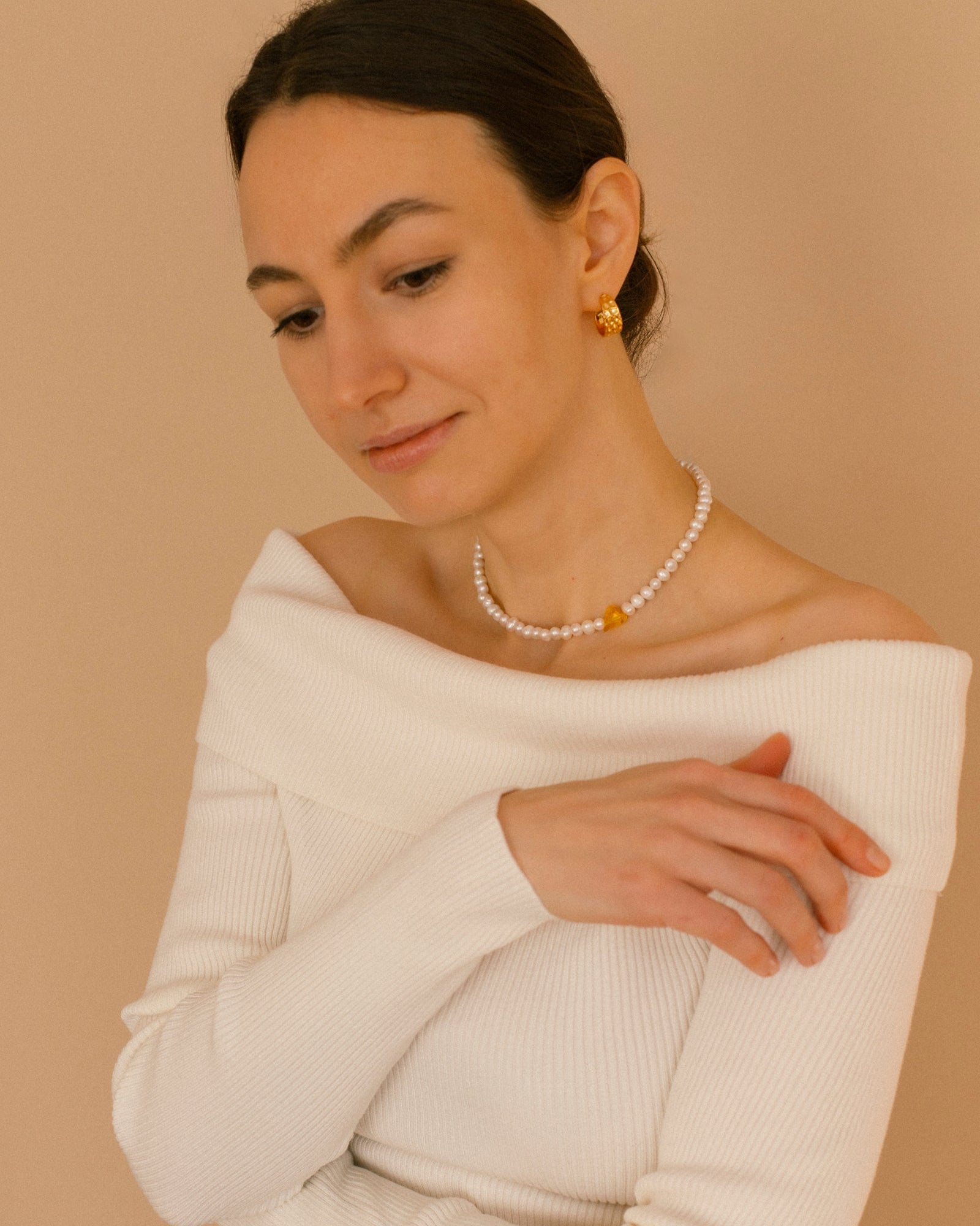Sweetheart pearl choker necklace with natural pearls and a yellow crystal heart, styled on model in elegant white off-shoulder top.