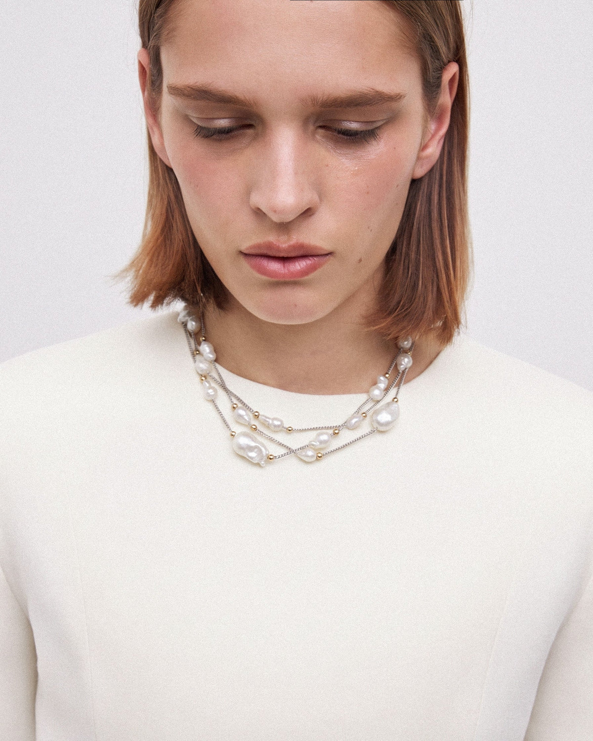 Model wearing a baroque pearl choker with three layered strands, silver-toned chains and small golden accents.