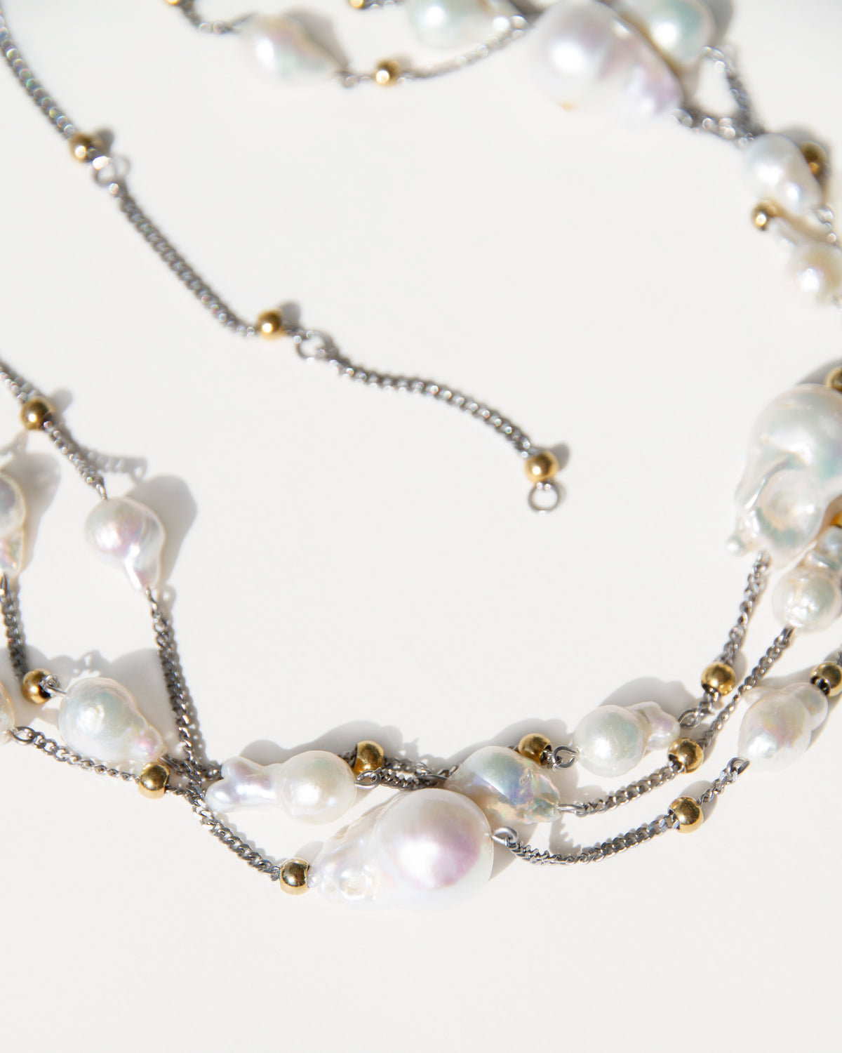 Close-up of irregular freshwater baroque pearls with fine silver-toned chains and small 18K gold-plated accents.