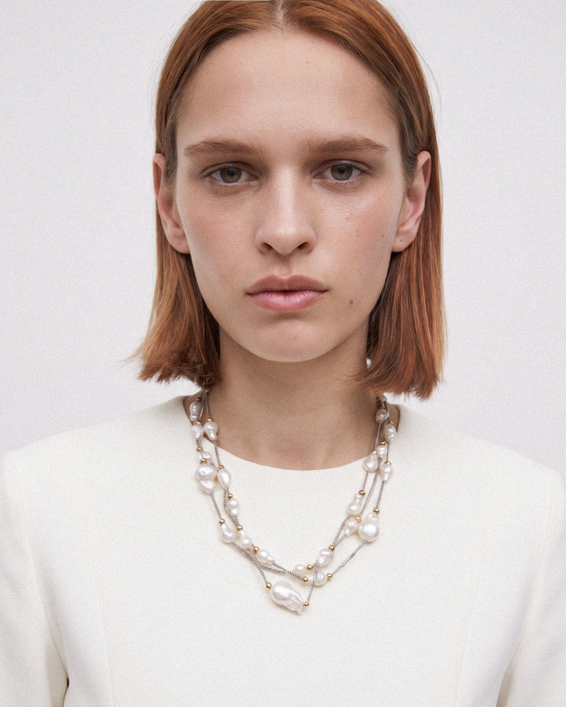 Model wearing a three-strand baroque pearl necklace in a longer, relaxed drape with silver and gold-toned details.