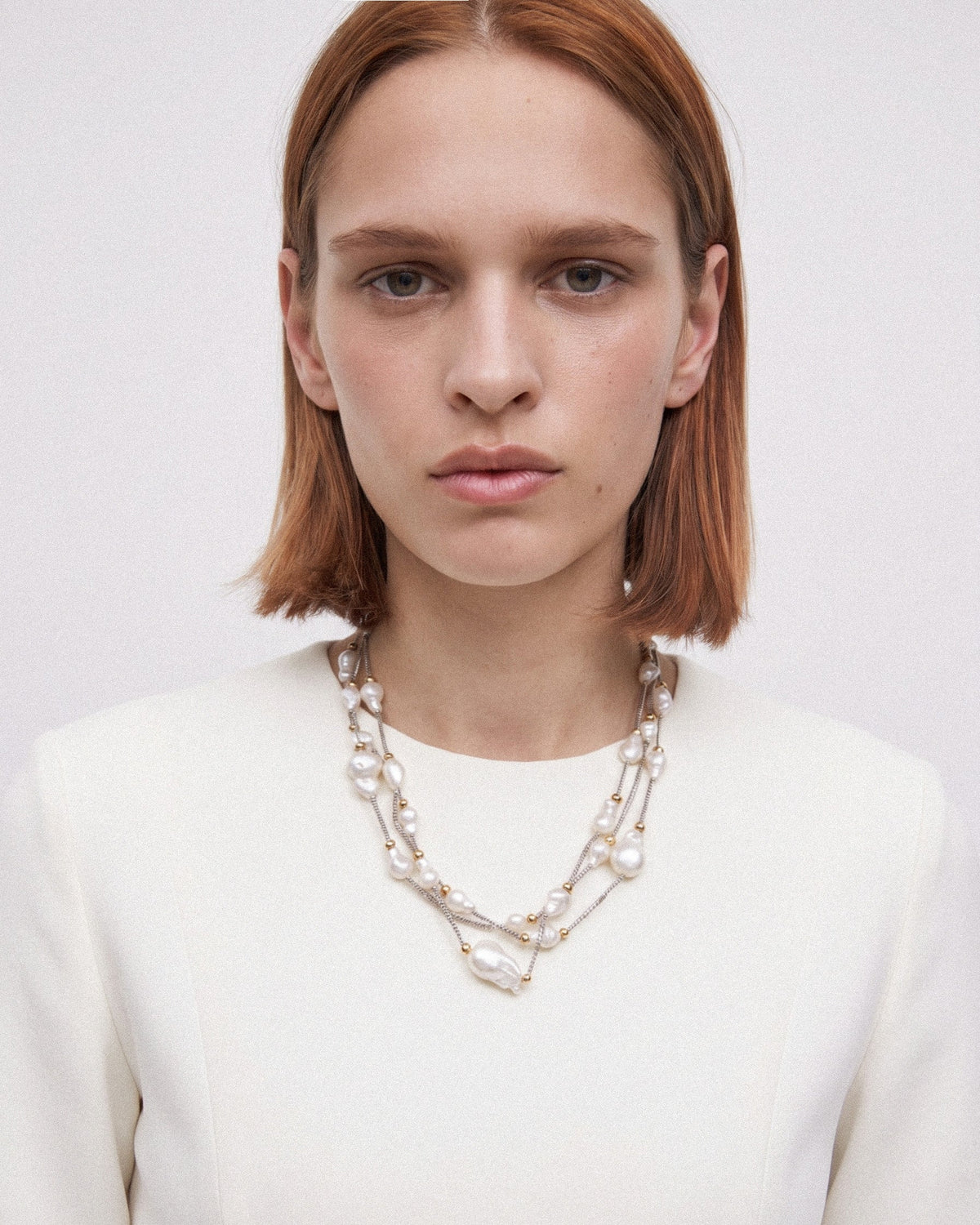Model wearing a three-strand baroque pearl necklace in a longer, relaxed drape with silver and gold-toned details.