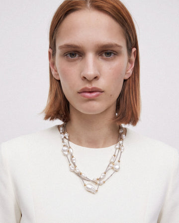 Model wearing a three-strand baroque pearl necklace in a longer, relaxed drape with silver and gold-toned details.