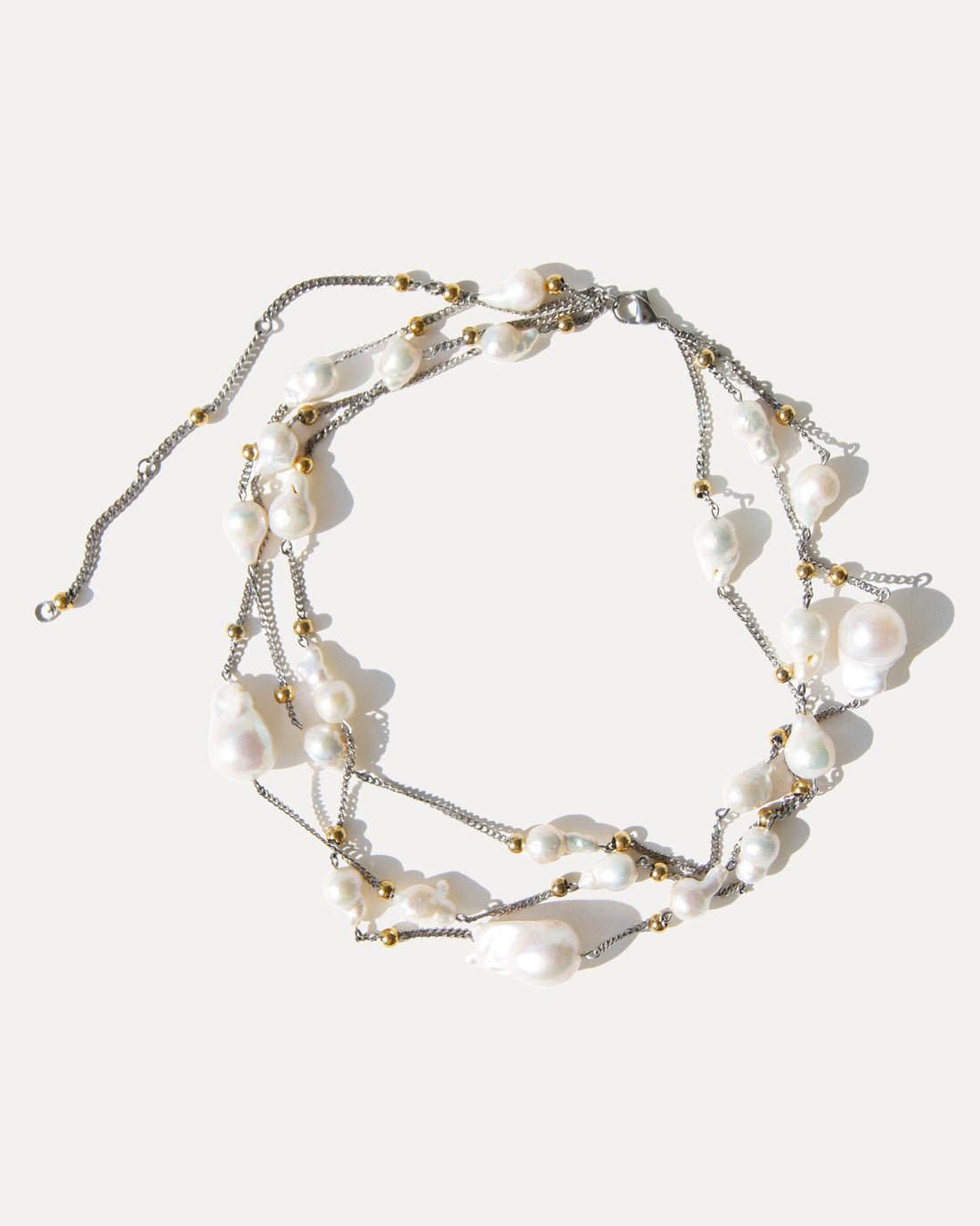 Model wearing a three-strand baroque pearl necklace in a longer, relaxed drape with silver and gold-toned details.