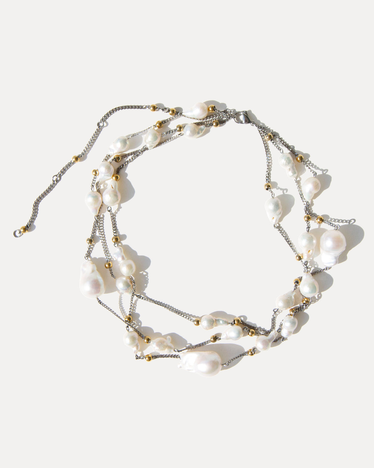 Three-strand baroque pearl necklace with mixed metal details, arranged in a loose, tangled composition on white.
