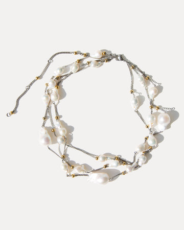 Three-strand baroque pearl necklace with mixed metal details, arranged in a loose, tangled composition on white.