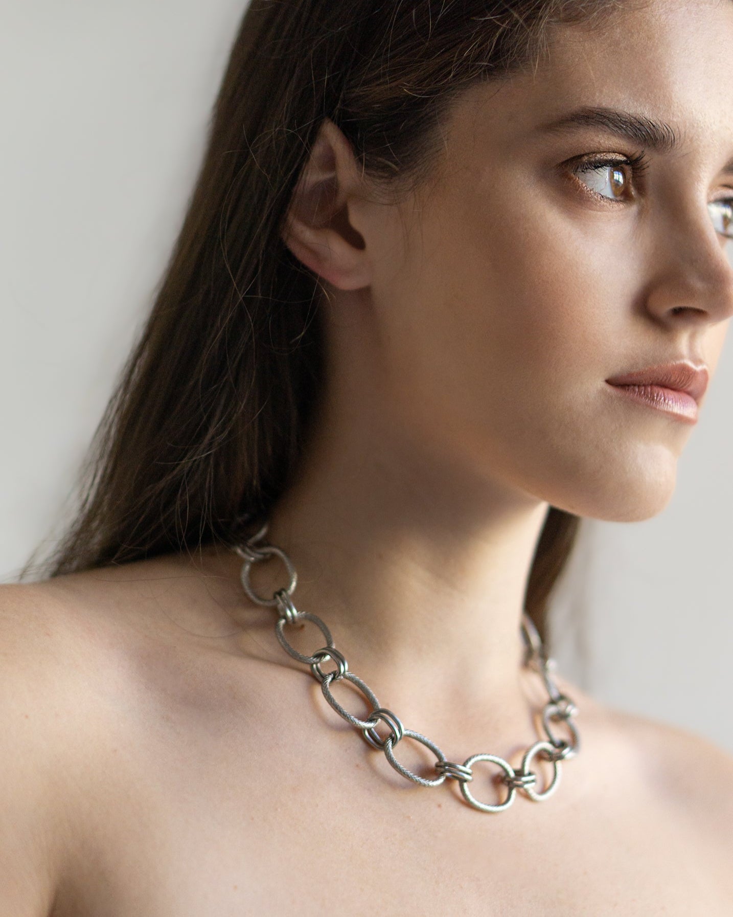 The Venus Necklace on model in profile — a sculptural stainless steel chain with airy oval links, balancing softness and structure in timeless design.