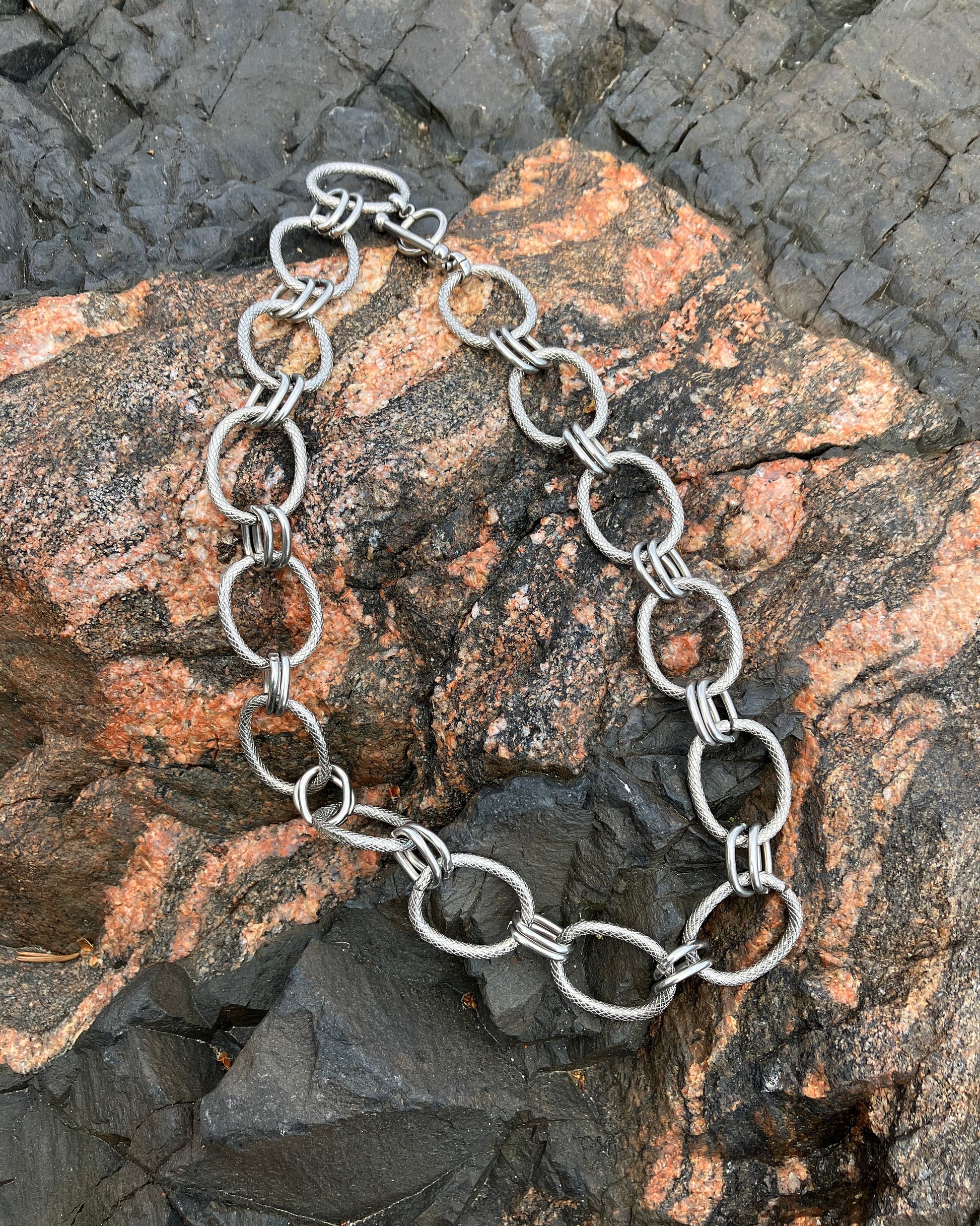 The Venus Necklace rests on textured stone, showing its sculptural stainless steel links — a modern statement chain with timeless edge and strength.