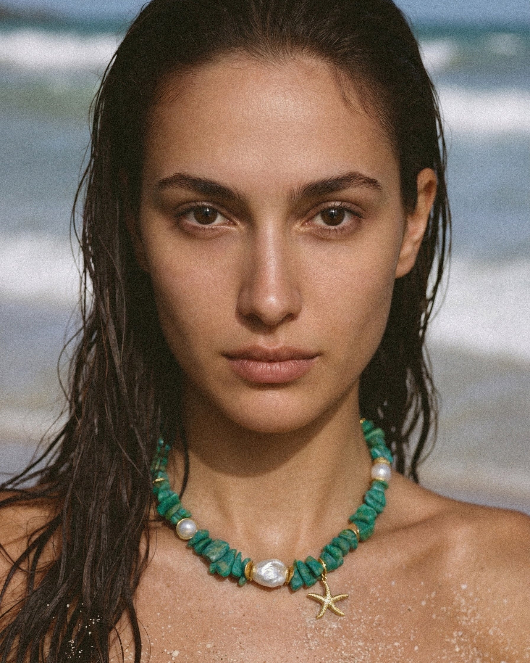 Model with wet hair wearing a green amazonite necklace with baroque freshwater pearls and a gold starfish charm by the sea.
